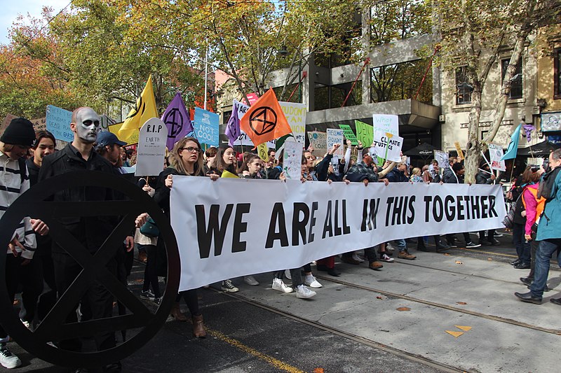 a group of protesters in a street holding a sign that reads: WE ARE ALL IN THIS TOGETHER